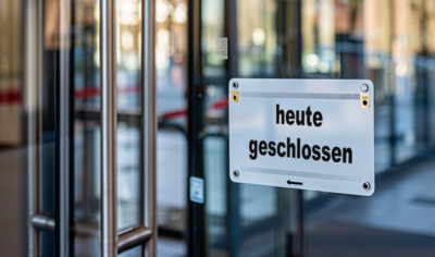 Auf dem Bild ist ein Eingang zu sehen, vermutlich zu einem öffentlichen Gebäude, möglicherweise einem Rathaus oder einer Behörde. Die Eingangstür besteht aus Glas und daneben steht ein Schild mit der Aufschrift „Heute geschlossen.“